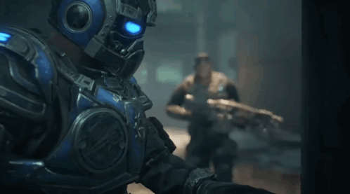 A Man In A Blue Armored Suit Is Holding A Gun GIF