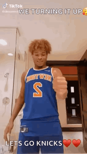 A Man In A Blue Basketball Jersey Is Giving A Thumbs Up In A Bathroom . GIF