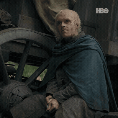 A Man In A Blue Cape Sits In Front Of A Wagon Wheel With The Hbo Logo On The Bottom GIF