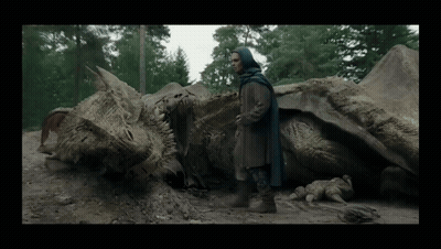 A Man In A Blue Cape Stands Next To A Dead Dragon In The Dirt GIF