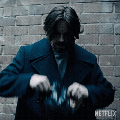 A Man In A Blue Coat Is Standing In Front Of A Brick Wall With A Netflix Logo Behind Him GIF