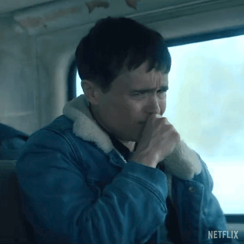 A Man In A Blue Denim Jacket Is Coughing While Sitting In Front Of A Window . GIF