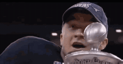 A Man In A Blue Hat Is Holding A Trophy In His Hand . GIF