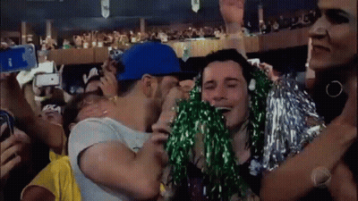 A Man In A Blue Hat Is Kissing A Woman In A Crowd . GIF