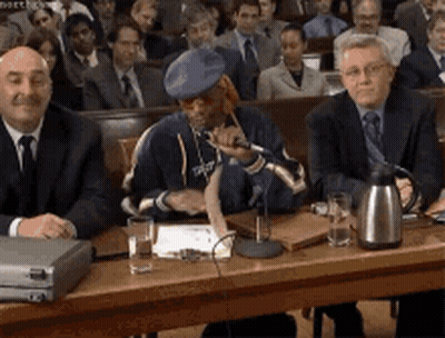 A Man In A Blue Hat Is Sitting At A Table With Other Men GIF