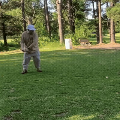 A Man In A Blue Hat Is Swinging A Golf Club On A Golf Course GIF