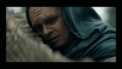 A Man In A Blue Hooded Cloak Is Laying On A Rock GIF