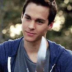 A Man In A Blue Hoodie Is Holding A Knife In His Hand And Smiling . GIF