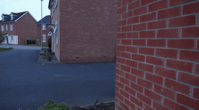 A Man In A Blue Hoodie Is Kneeling Down In Front Of A Brick Building GIF