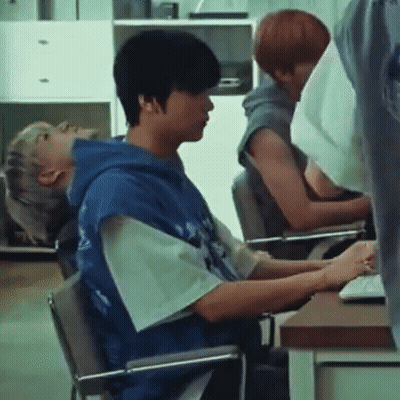 A Man In A Blue Hoodie Is Sitting In A Chair In Front Of A Computer . GIF