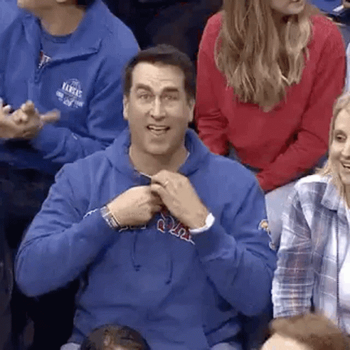 A Man In A Blue Hoodie Is Sitting In A Crowd Of People Watching A Game . GIF