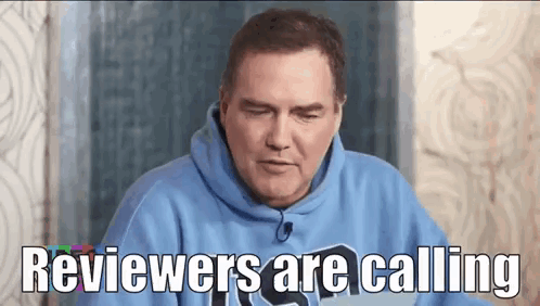A Man In A Blue Hoodie Is Sitting In Front Of A Laptop Computer And Says Reviewers Are Calling . GIF