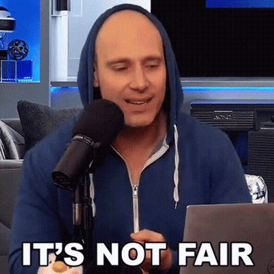A Man In A Blue Hoodie Is Sitting In Front Of A Microphone With The Words " It 'S Not Fair " On The Bottom GIF