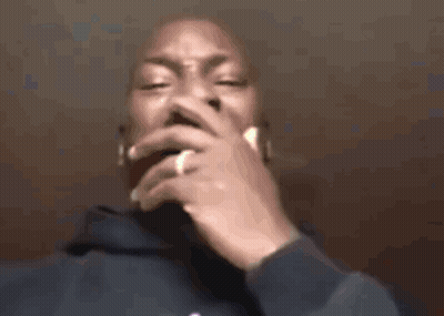 A Man In A Blue Hoodie Is Smoking A Cigarette With His Hand On His Mouth . GIF