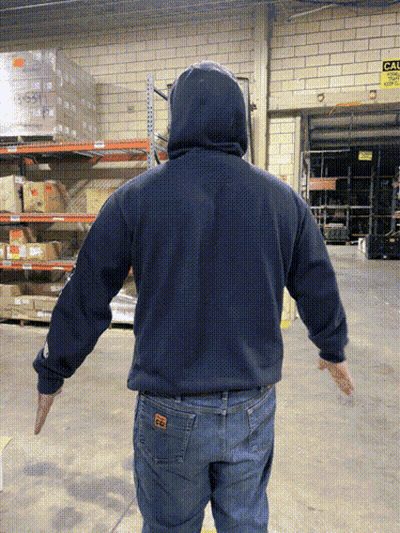 A Man In A Blue Hoodie Is Standing In A Warehouse With His Arms Outstretched In Front Of A Sign That Says Exit GIF