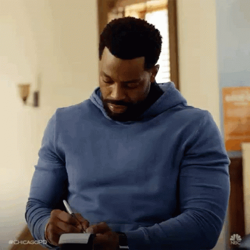 A Man In A Blue Hoodie Is Taking Notes In A Notebook . GIF