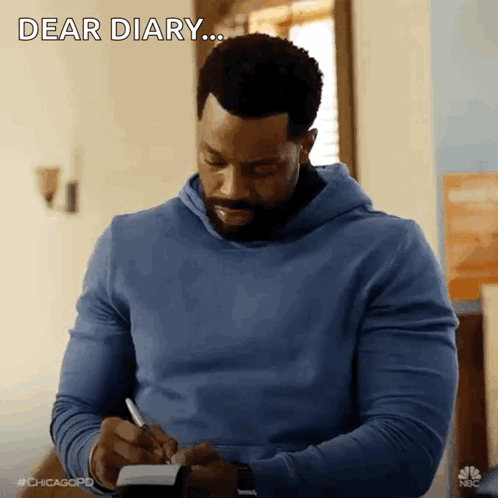 A Man In A Blue Hoodie Is Writing In A Notebook And Saying Dear Diary GIF