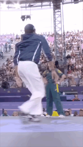 A Man In A Blue Jacket And White Pants Is Riding A Skateboard In Front Of A Crowd GIF
