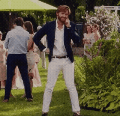 A Man In A Blue Jacket And White Pants Is Standing In A Grassy Field Talking On A Cell Phone . GIF