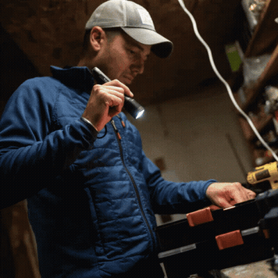 A Man In A Blue Jacket Holds A Flashlight In His Hand GIF