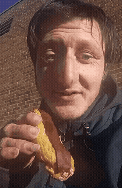 A Man In A Blue Jacket Is Eating A Sandwich GIF