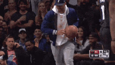 A Man In A Blue Jacket Is Holding A Basketball In Front Of A Crowd With The Number 11 On His Jersey GIF