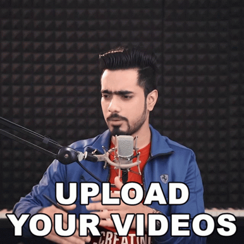 A Man In A Blue Jacket Is Holding A Microphone With The Words Upload Your Videos Above Him GIF