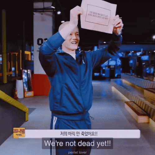 A Man In A Blue Jacket Is Holding Up A Piece Of Paper That Says We 'Re Not Dead Yet GIF