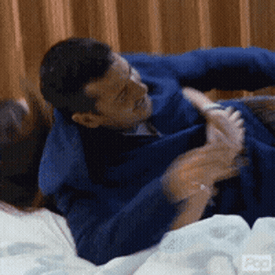A Man In A Blue Jacket Is Laying On A Bed Holding A Woman 'S Hand GIF