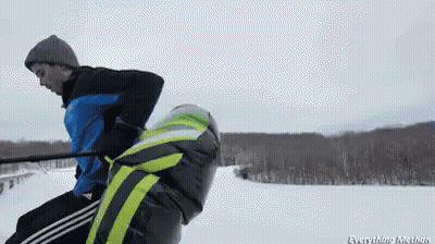 A Man In A Blue Jacket Is Pulling Another Man On A Sled GIF