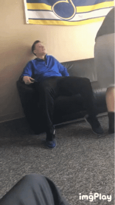 A Man In A Blue Jacket Is Sitting On A Black Couch In Front Of A Banner That Says Tm GIF