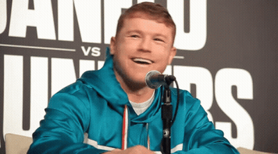 A Man In A Blue Jacket Is Smiling In Front Of A Microphone In Front Of A Sign That Says Vs GIF