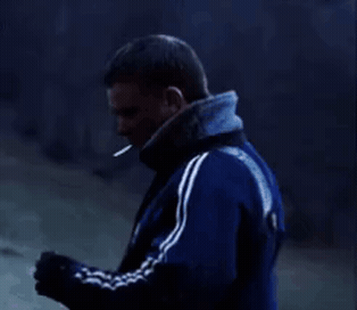 A Man In A Blue Jacket Is Smoking A Cigarette While Standing In The Dark . GIF