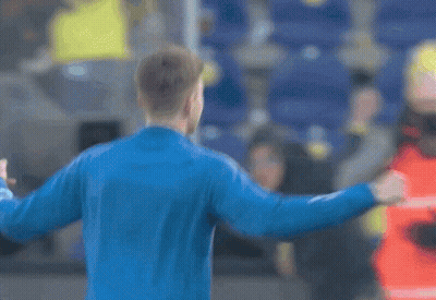 A Man In A Blue Jacket Is Standing In Front Of A Crowd With His Fist In The Air GIF