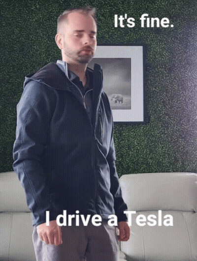 A Man In A Blue Jacket Is Standing In Front Of A Picture That Says I Drive A Tesla GIF