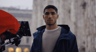 A Man In A Blue Jacket Is Standing In Front Of A Red Camera GIF