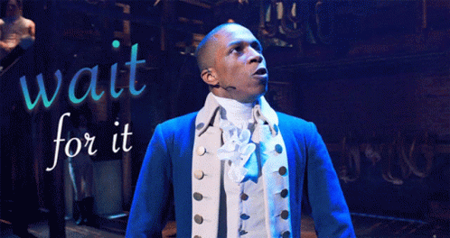 A Man In A Blue Jacket Is Standing In Front Of A Sign That Says Wait For It GIF