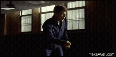 A Man In A Blue Jacket Is Standing In Front Of A Window In A Room . GIF