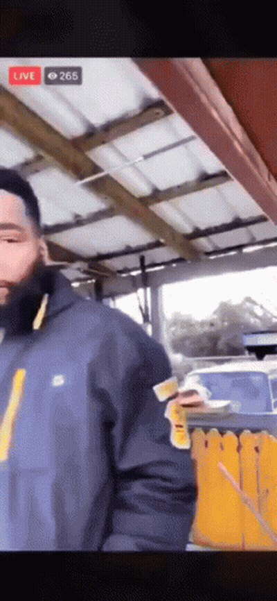 A Man In A Blue Jacket Is Standing In Front Of A Yellow Fence While Holding A Piece Of Paper . GIF