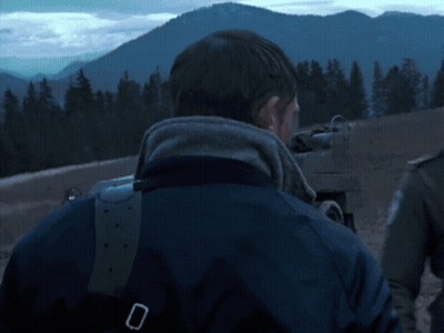 A Man In A Blue Jacket Is Standing In Front Of Mountains GIF