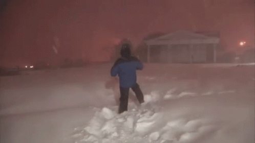 A Man In A Blue Jacket Is Standing In The Snow In Front Of A House GIF