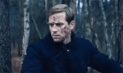 A Man In A Blue Jacket Is Standing In The Woods With Blood On His Face . GIF