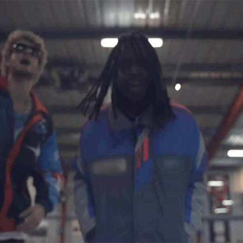A Man In A Blue Jacket Is Standing Next To Another Man In A Red Vest . GIF