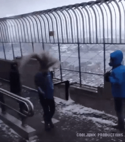 A Man In A Blue Jacket Is Throwing Snow At Another Man In A Blue Jacket GIF