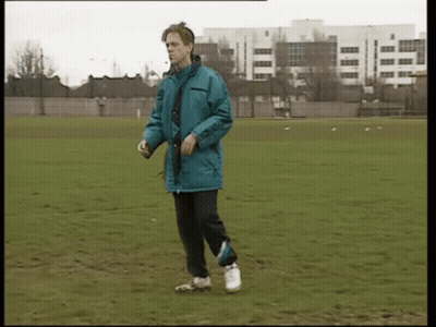 A Man In A Blue Jacket Is Walking On A Grassy Field GIF
