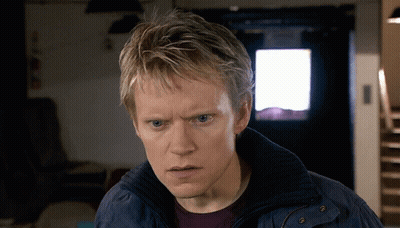 A Man In A Blue Jacket Looks At The Camera With A Serious Look On His Face GIF