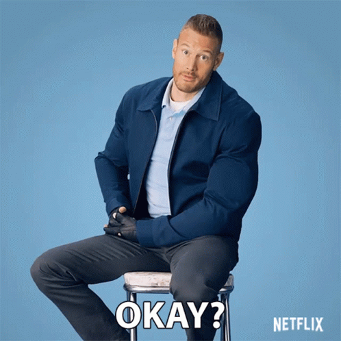 A Man In A Blue Jacket Sits On A Stool With Okay Written On The Bottom GIF