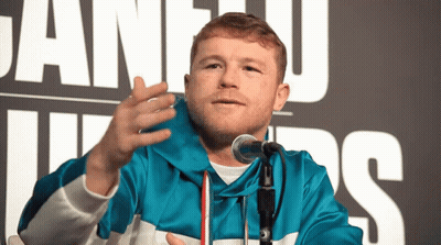 A Man In A Blue Jacket Speaking Into A Microphone In Front Of A Sign That Says Juan Luis GIF