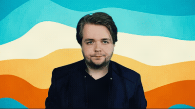 A Man In A Blue Jacket Stands In Front Of A Rainbow Colored Background GIF