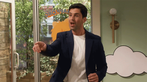 A Man In A Blue Jacket Stands In Front Of A Sign That Says ' Dinosaur ' On It GIF